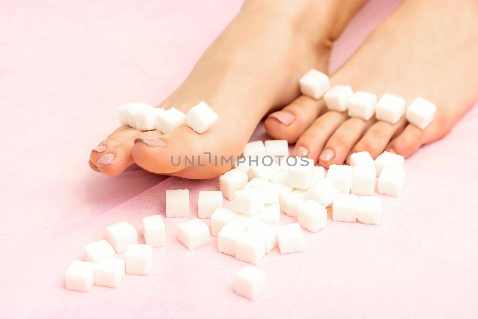 Sugar cubes lying in a row on female feet on pink background with copy space, depilation concept