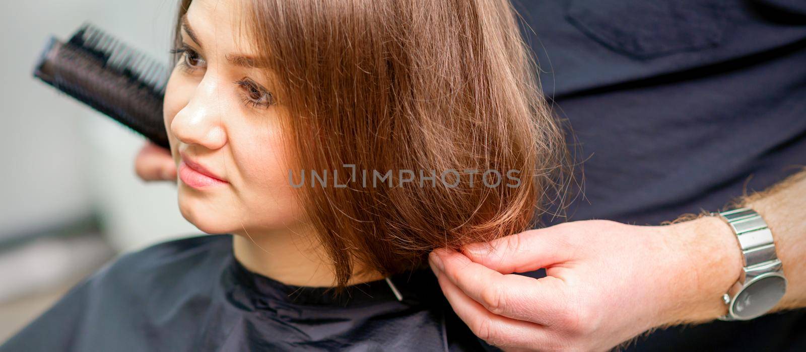 Styling female hair. Male hairdresser makes hairstyle for a young woman in a beauty salon. by okskukuruza