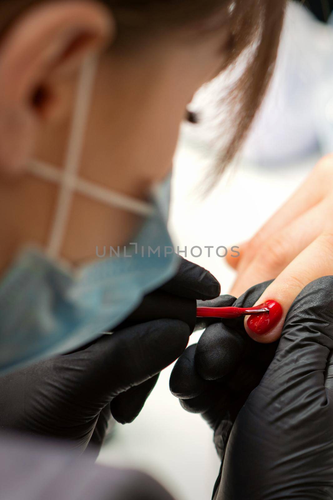 Painting nails of a woman. Hands of Manicurist in black gloves applying red nail polish on female Nails in a beauty salon. by okskukuruza