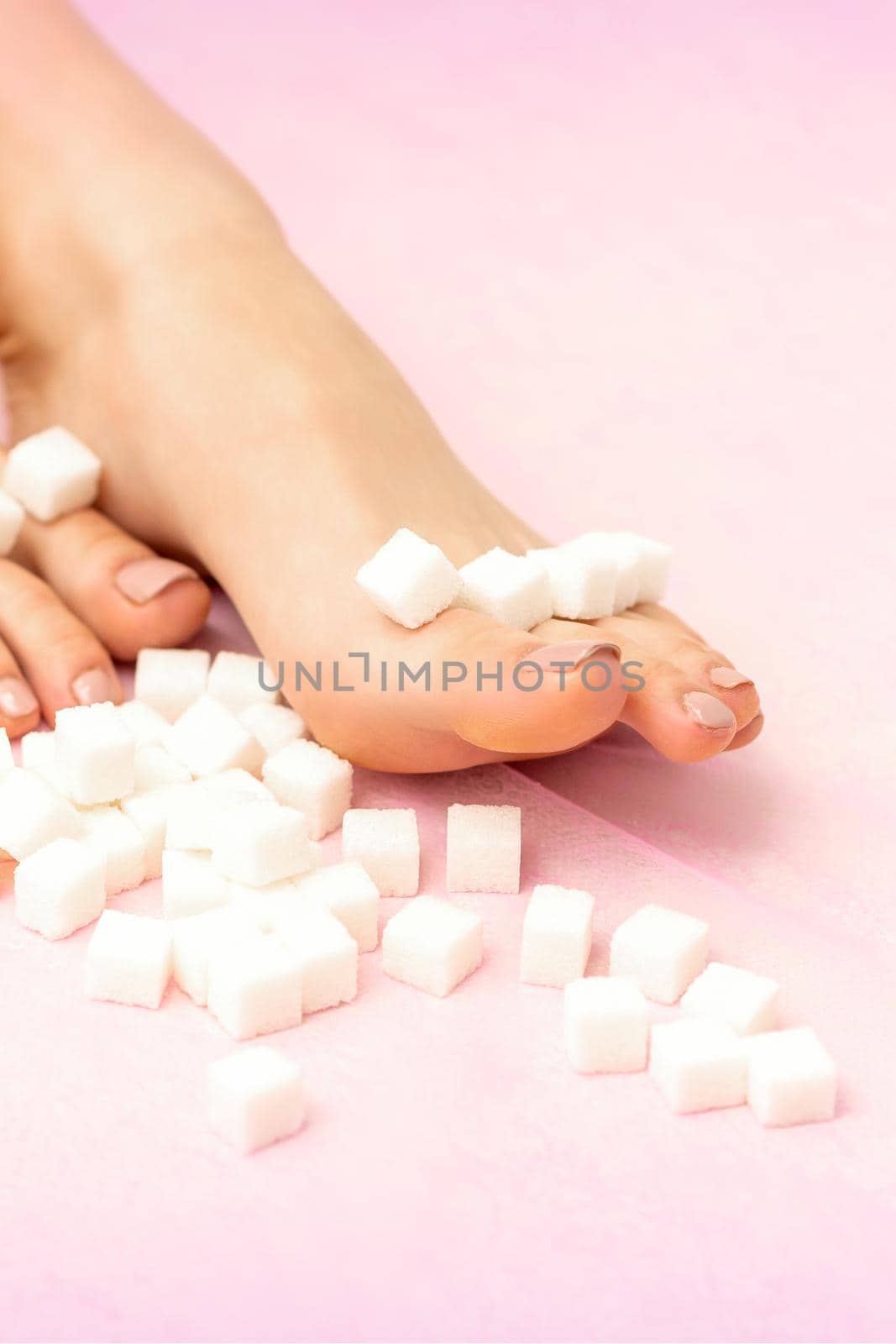 Sugar cubes lying in a row on female feet on pink background with copy space, depilation concept. by okskukuruza