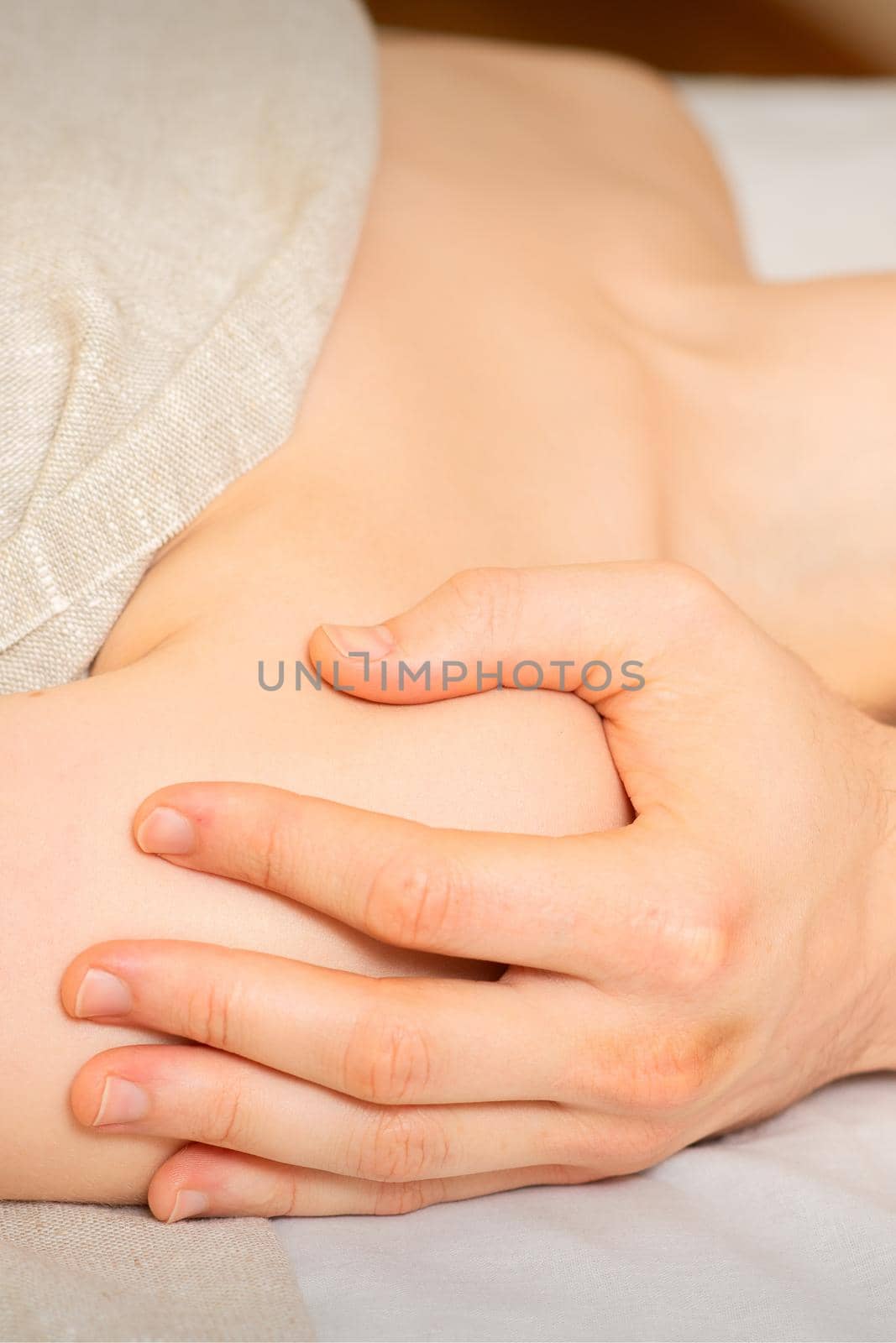Male masseur massaging shoulder of a young woman lying on a massage table in a spa clinic