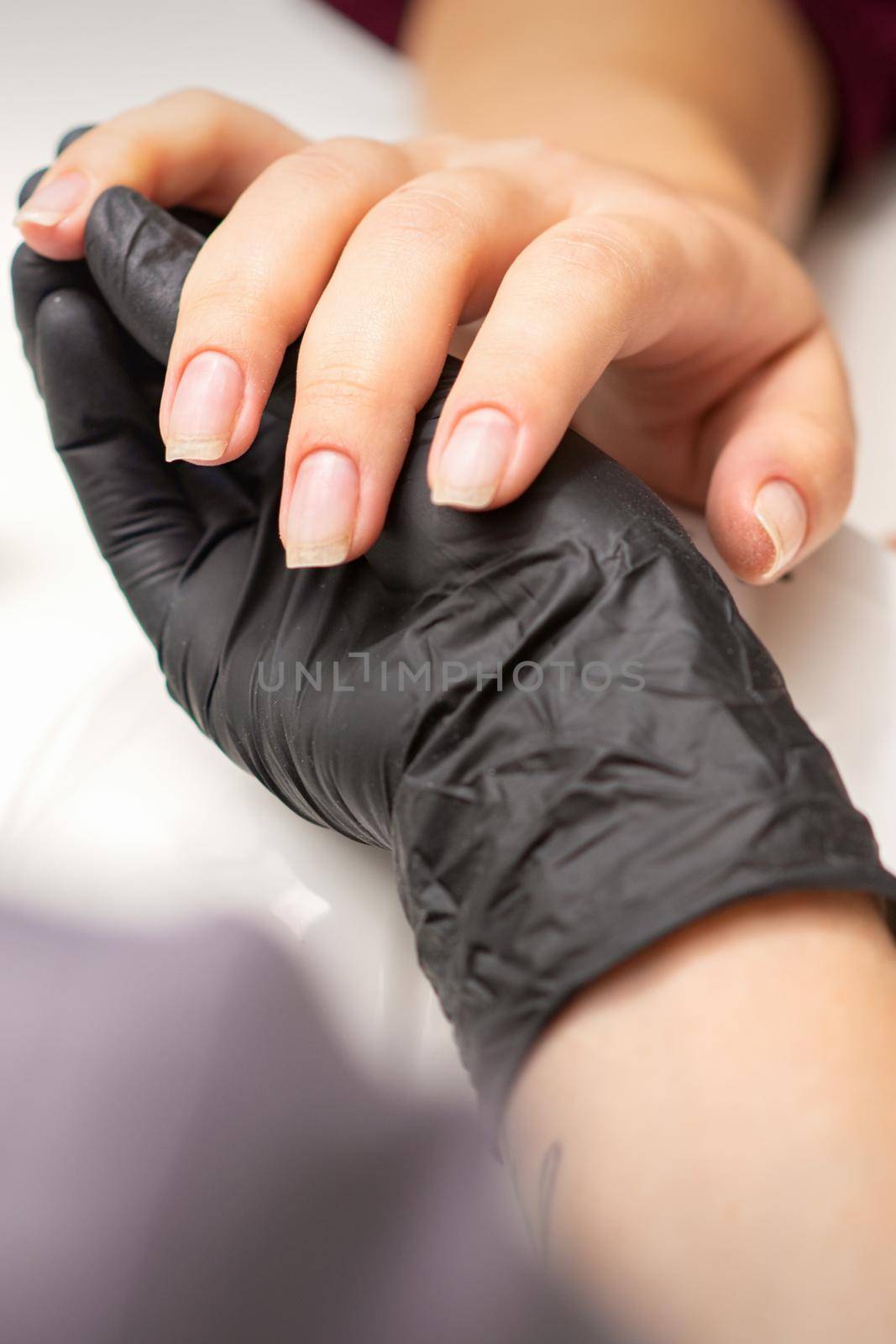 Examination of manicured fingernails. Hands of manicure master in black gloves examining female transparent nails in manicure salon. by okskukuruza