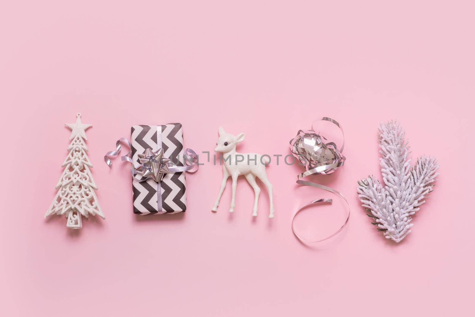 Festive minimal creative christmas composition with gift, deer, xmas tree flat lay on pink background.