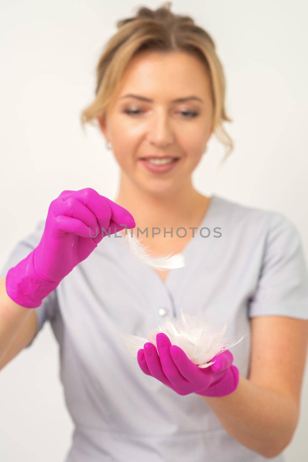 The beautician holds white feathers in her gloved hands over white background. Concept of health softness skin and body care