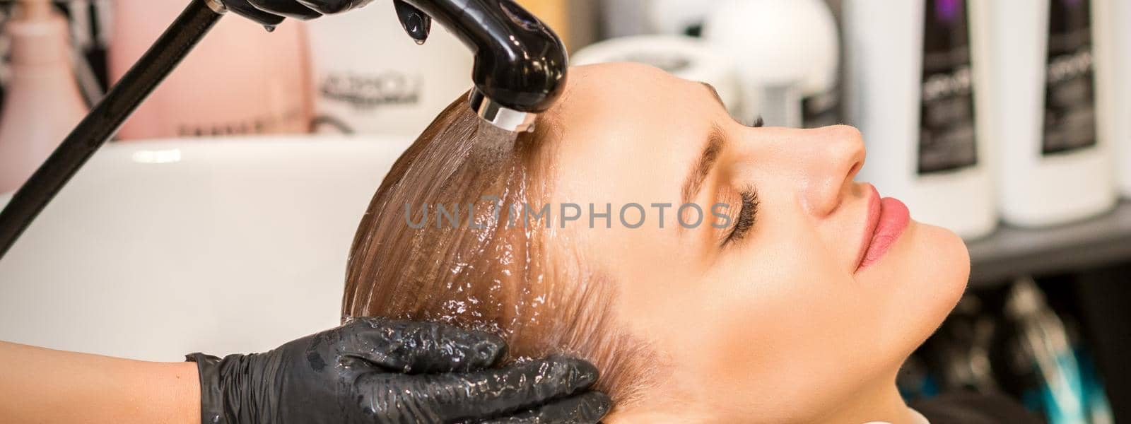 Young caucasian blonde woman having hair washed in the sink at a beauty salon. by okskukuruza