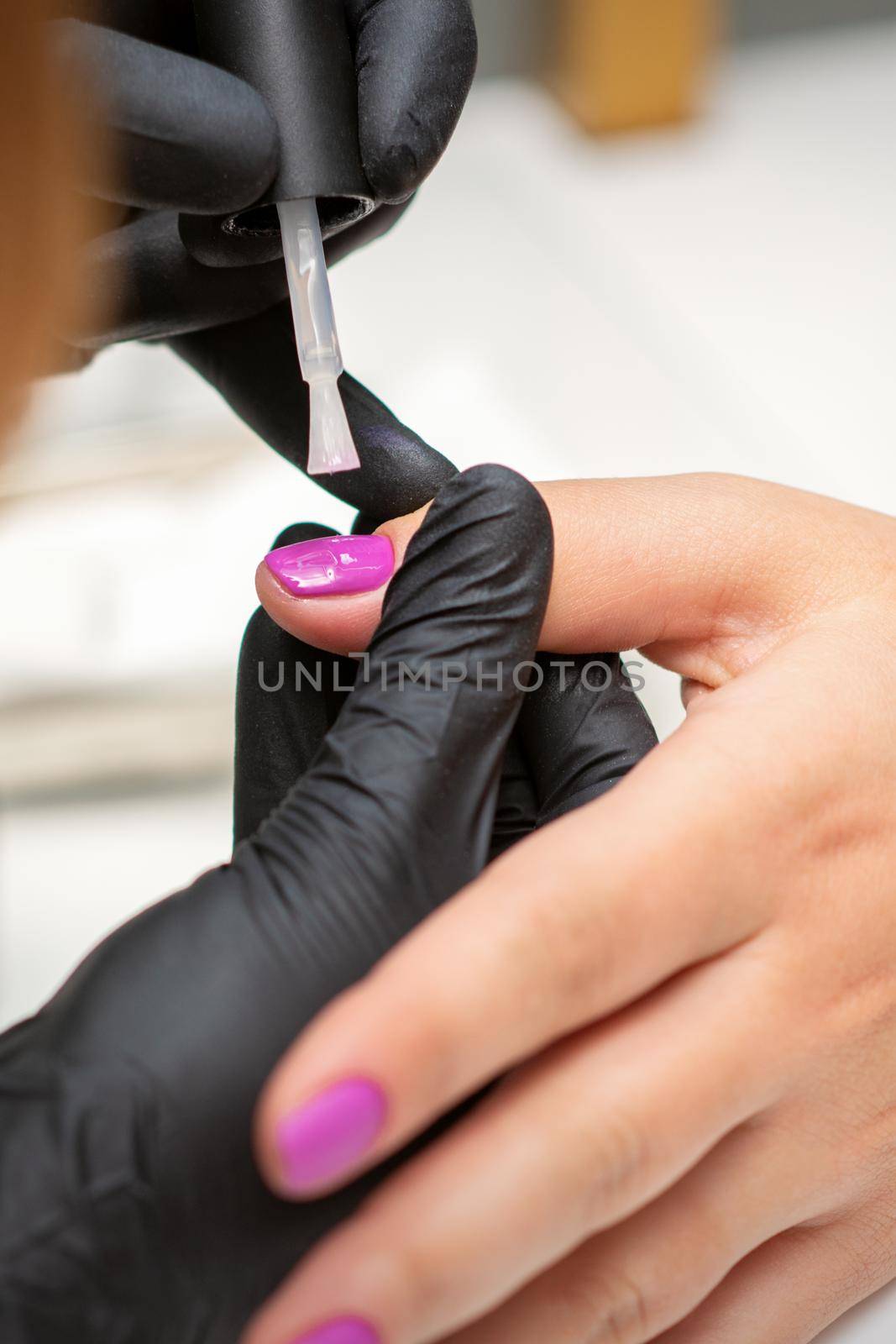 Painting nails of a woman. Hands of Manicurist in black gloves applying pink nail polish on female Nails in a beauty salon. by okskukuruza