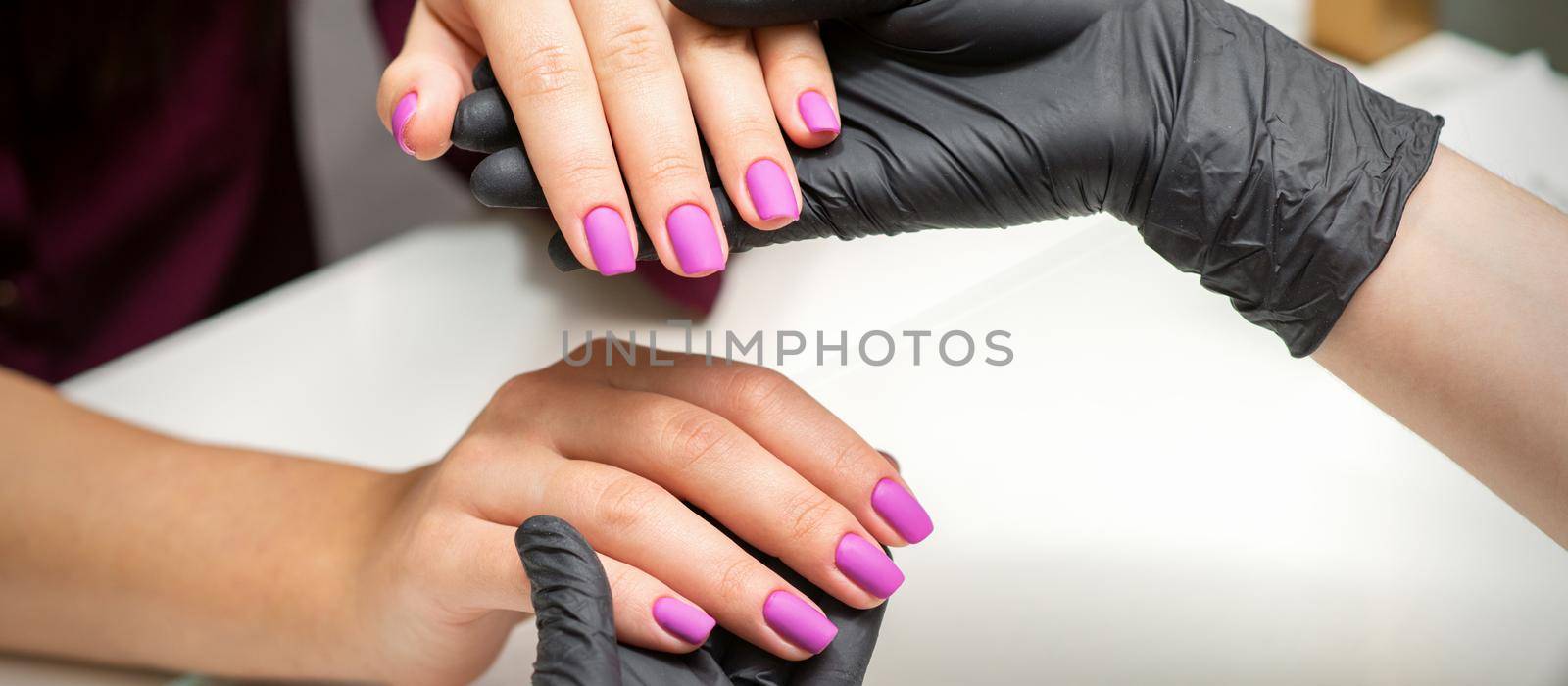 Examination of manicured fingernails. Hands of manicure master in black gloves examining female pink nails in manicure salon