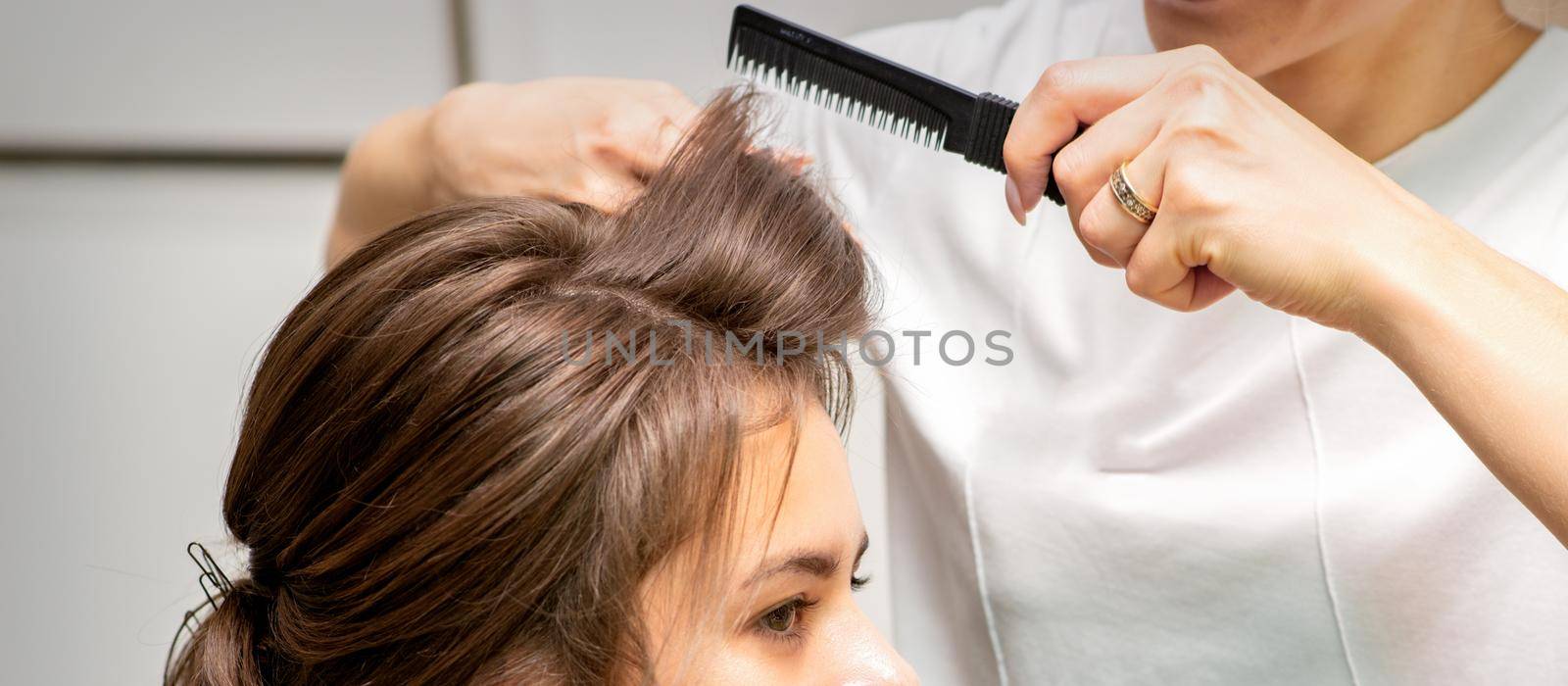 Professional hairdresser doing hairstyle for a beautiful brunette young woman with long hair. Concept of fashion and beauty