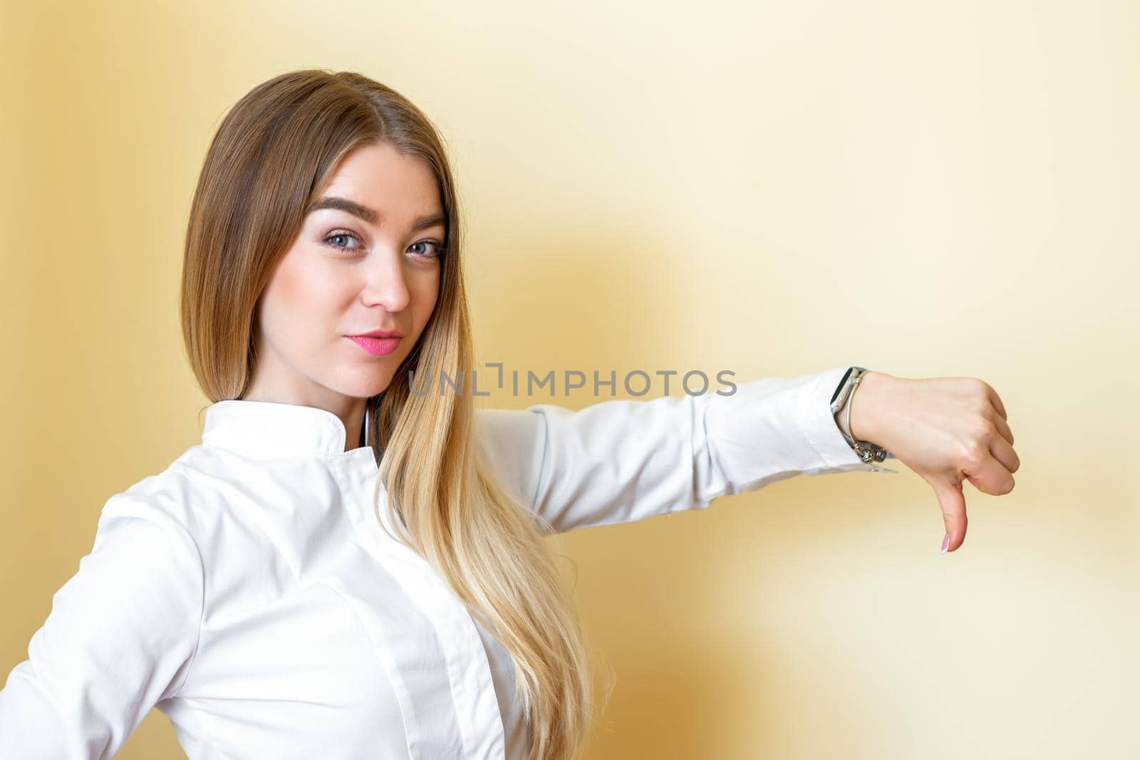 A woman showing dislike. Young beautiful businesswoman wearing a white shirt with thumb down isolated over a yellow background