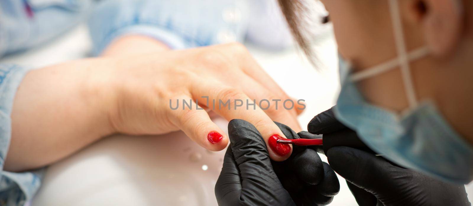 Painting nails of a woman. Hands of Manicurist in black gloves applying red nail polish on female Nails in a beauty salon. by okskukuruza