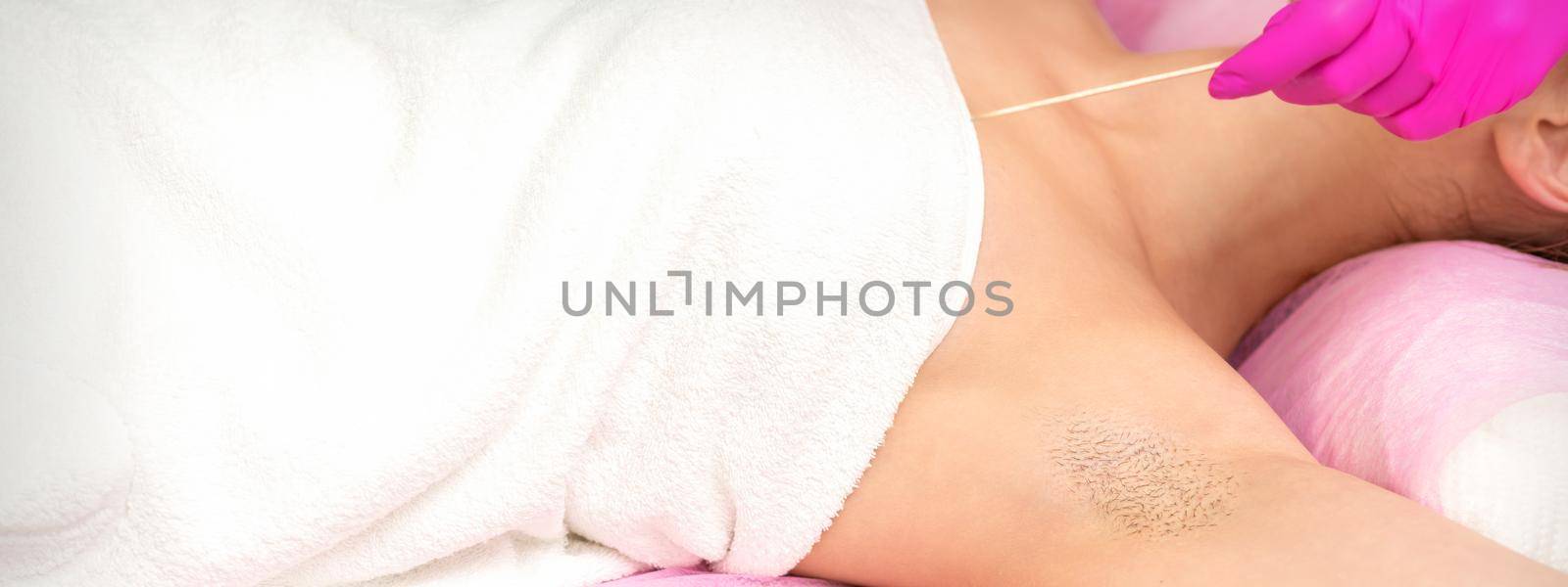 Hand in glove with spatula depilates female hairy armpit in a spa
