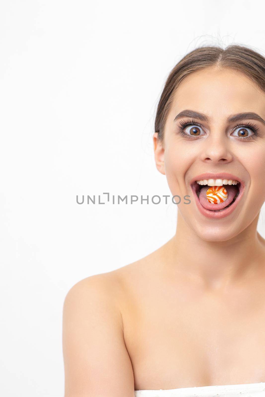 Happy expression young nude woman with candy in mouth on white background, epilation, depilation, hair removal concept