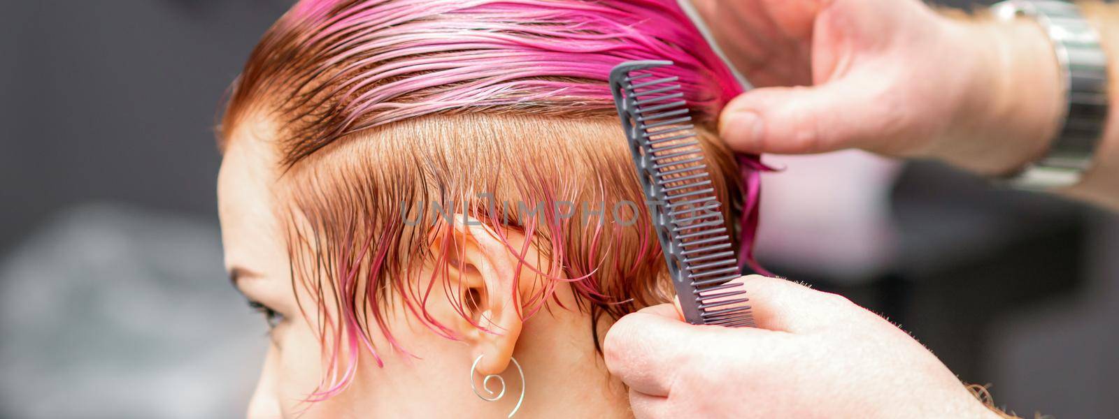 Styling female hair. Male hairdresser makes hairstyle for a young woman in a beauty salon