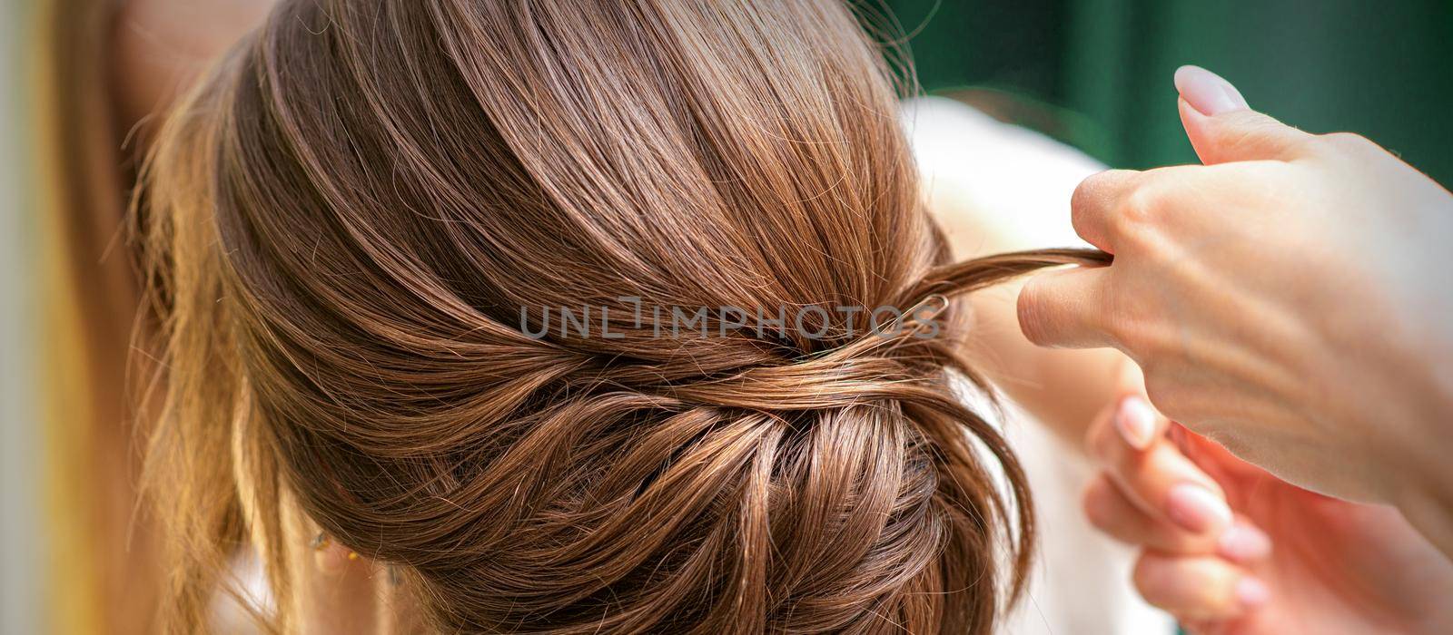 Professional hairdresser doing hairstyle for a beautiful brunette young woman with long hair. Concept of fashion and beauty