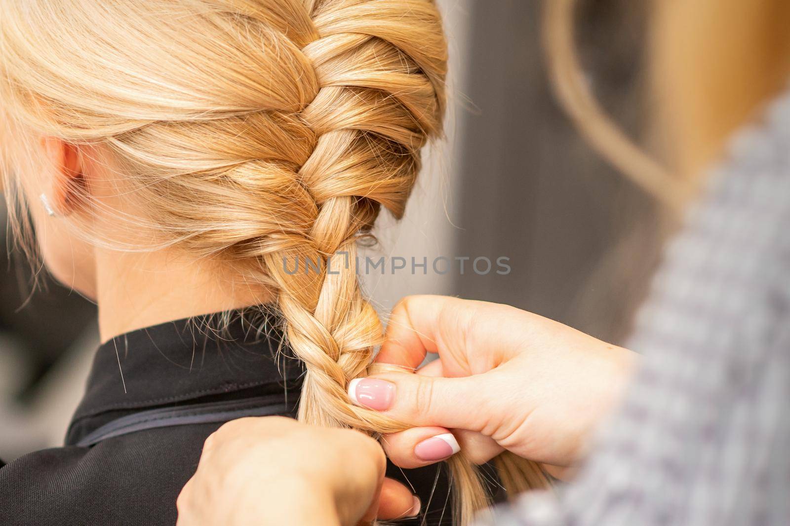Braiding braid. Hands of female hairdresser braids long braid for a blonde woman in a hair salon