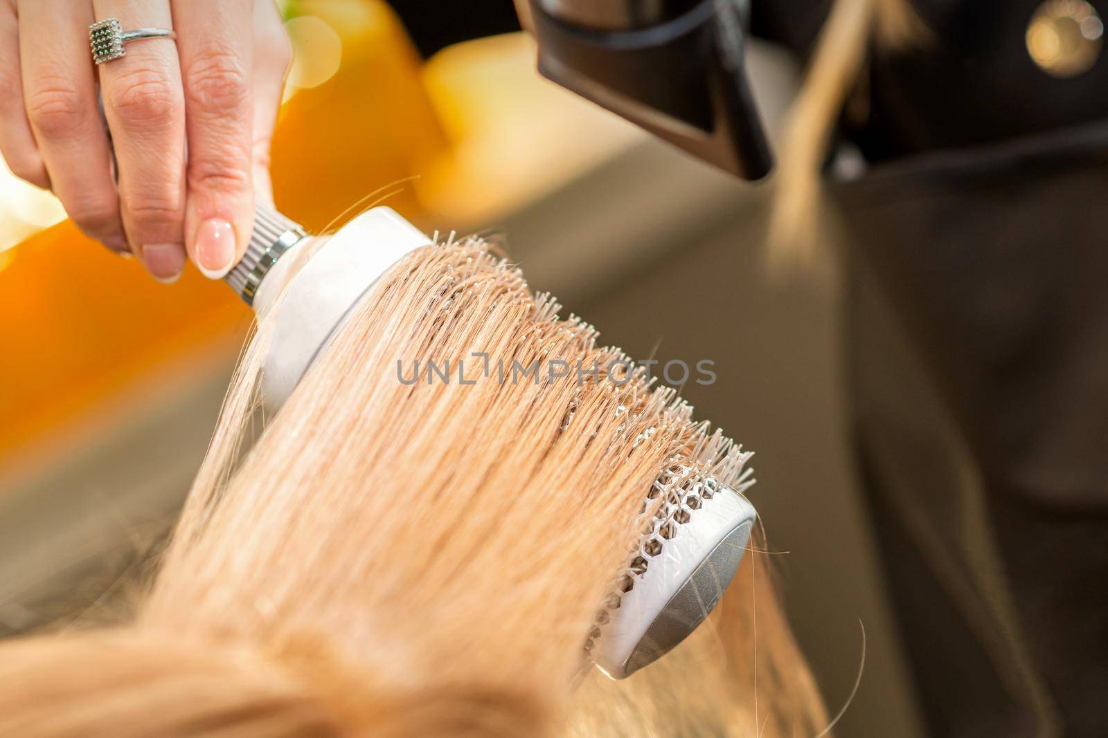 Hairdresser hand drying blond hair with a hairdryer and round brush in a beauty salon