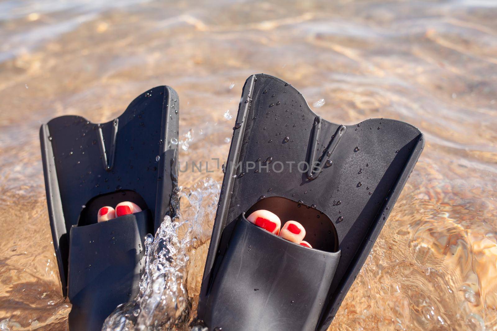 A woman in black flippers splashes near the shore. Fins stick out by AnatoliiFoto