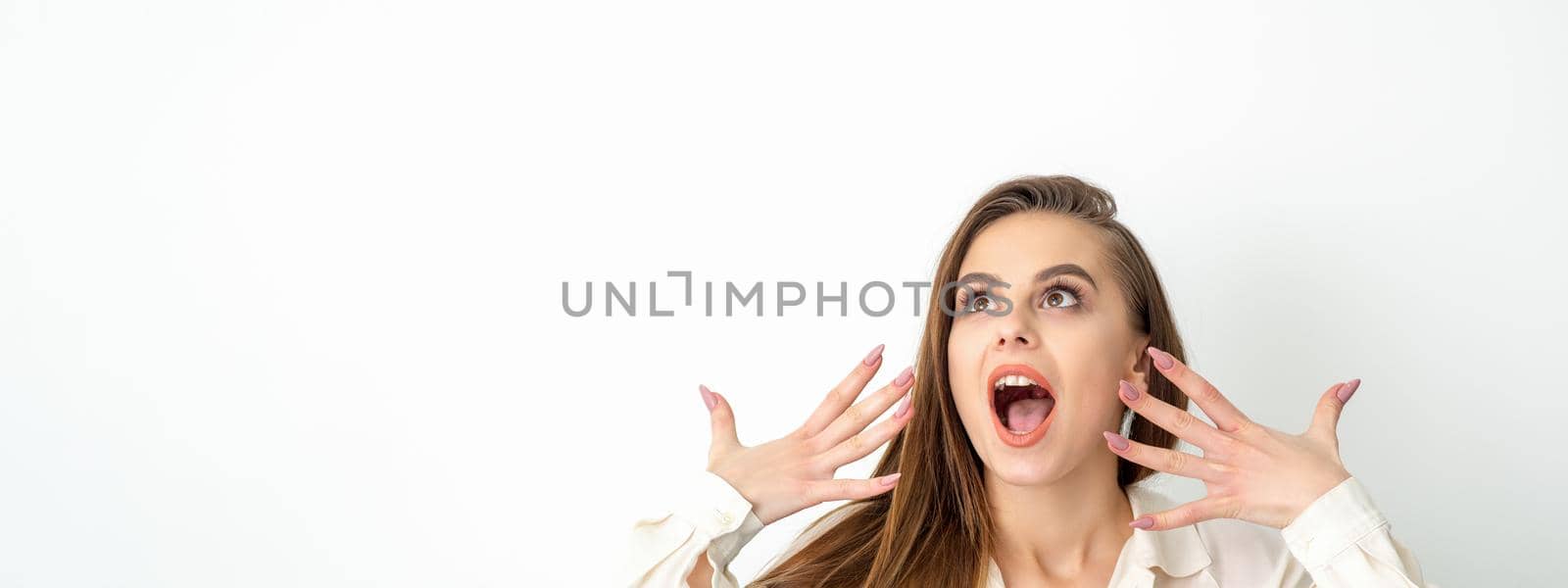 Shocked young caucasian woman with open mouth looking up and expresses surprise isolated over white background. Beautiful surprised brunette woman in studio
