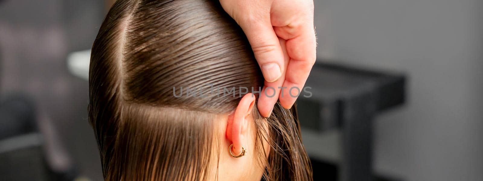 Hairdresser divides female hair into sections with comb holding hair with her hands in hair salon close up