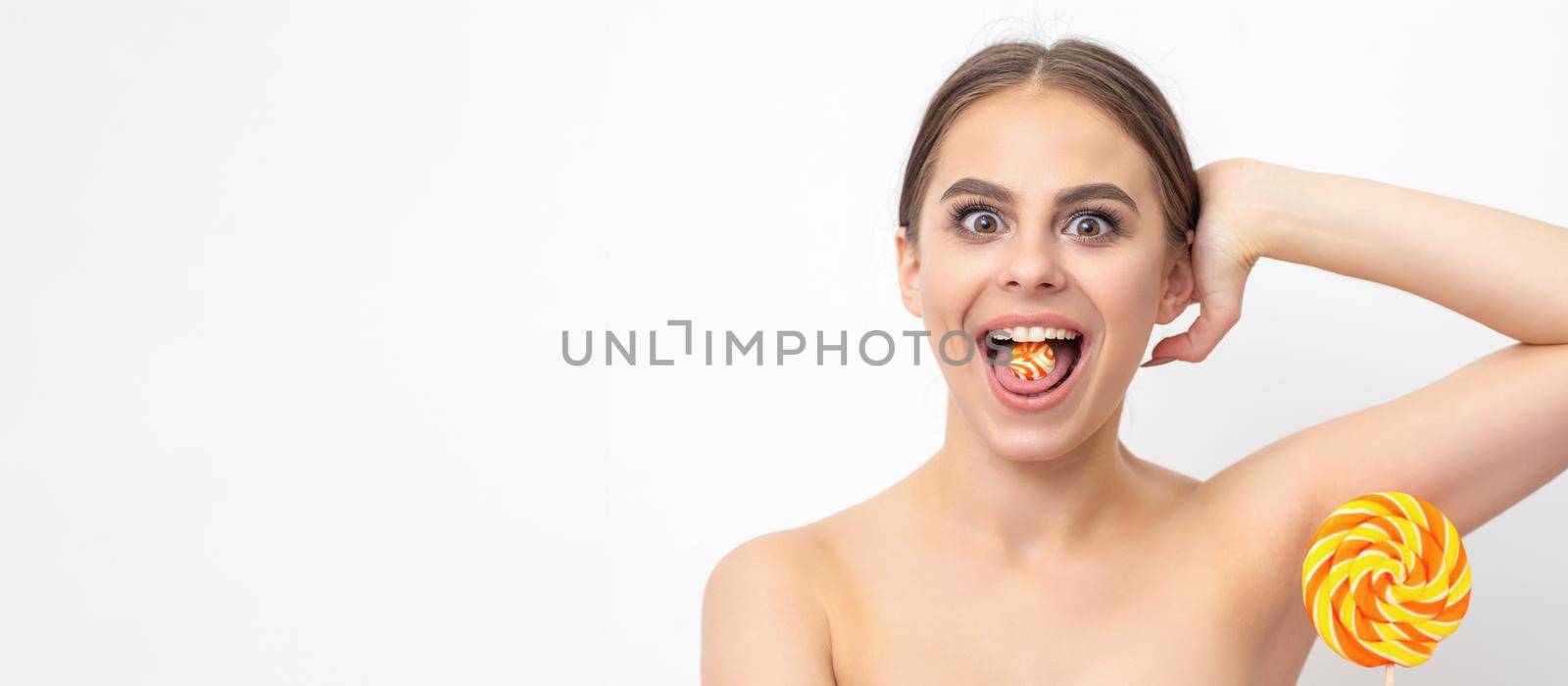 Happy expression young nude woman with candy in mouth holds lollipop near armpit on white background, epilation, depilation, hair removal concept