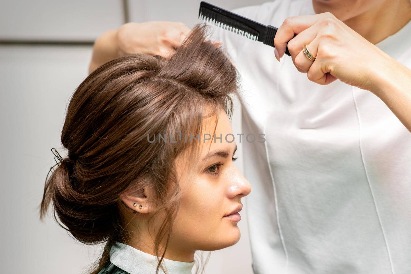 Professional hairdresser doing hairstyle for a beautiful brunette young woman with long hair. Concept of fashion and beauty