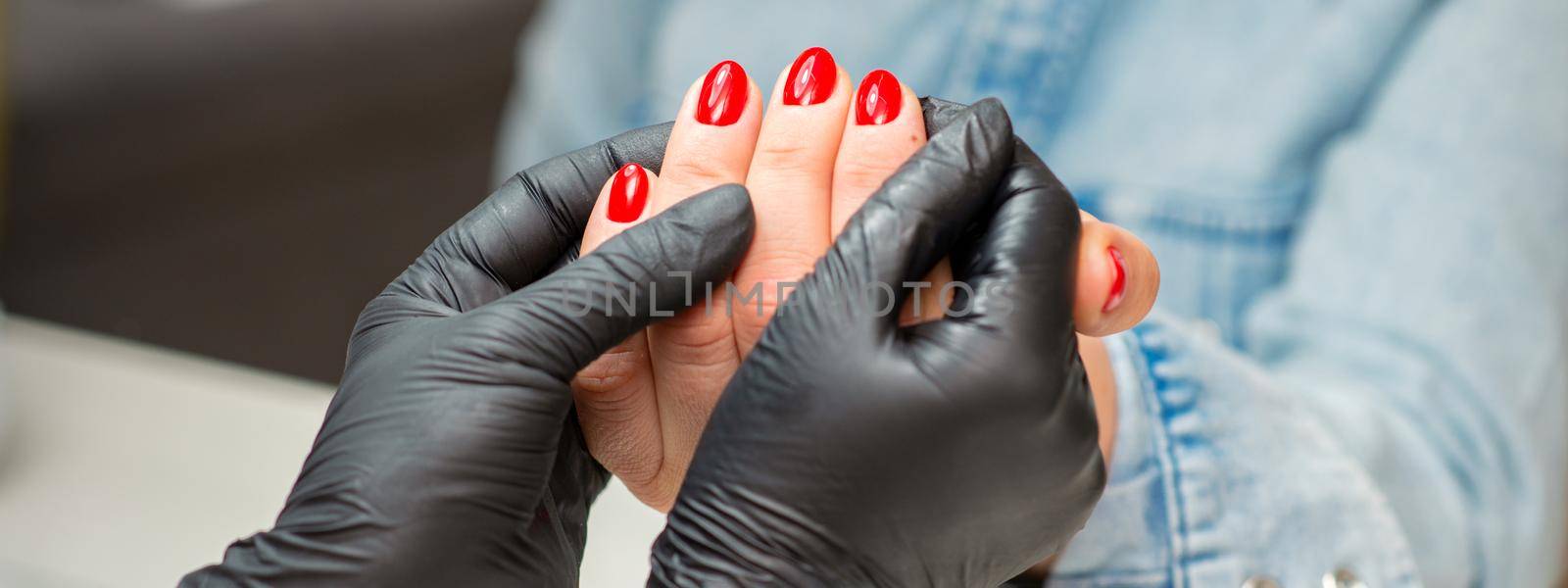 Examination of manicured fingernails. Hands of manicure master in black gloves examining female red nails in manicure salon. by okskukuruza
