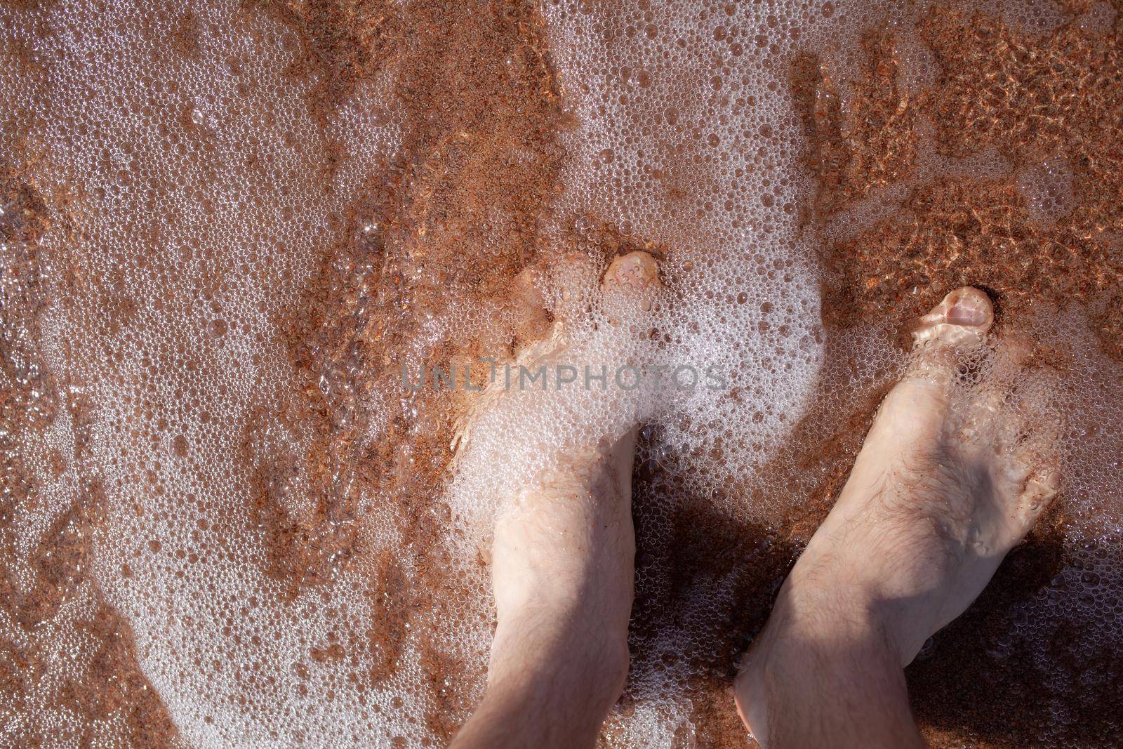 Top view of men's legs in the sea. A man is standing on the sand. by AnatoliiFoto