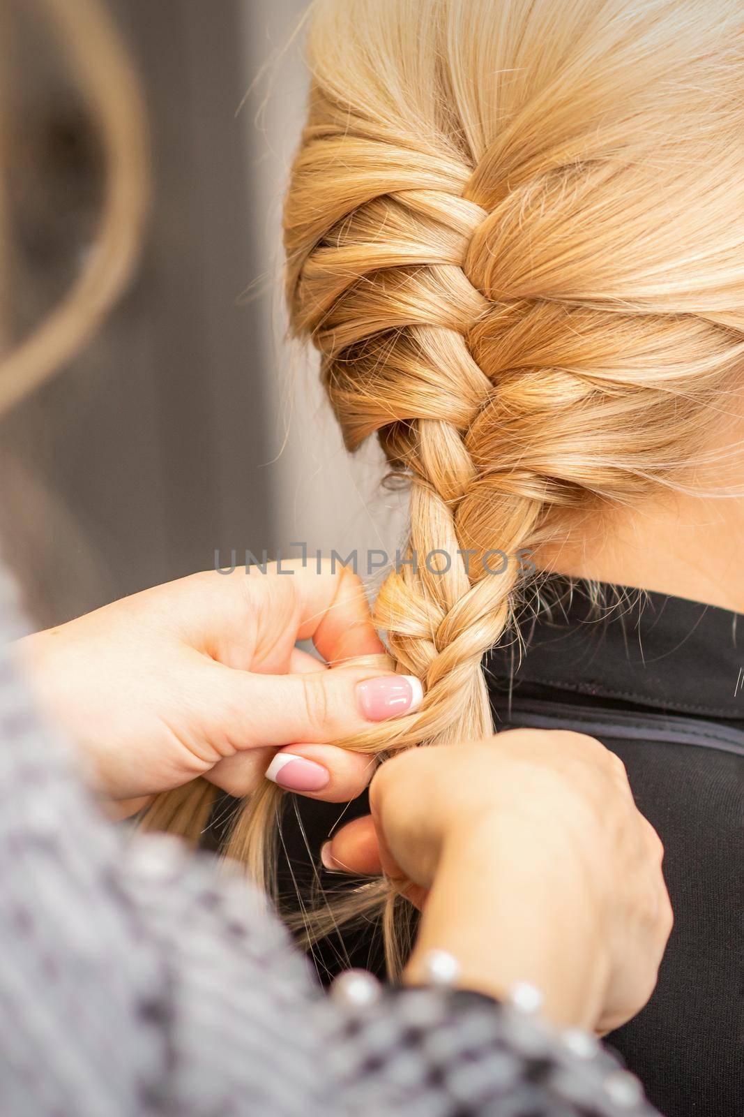 Braiding braid. Hands of female hairdresser braids long braid for a blonde woman in a hair salon. by okskukuruza