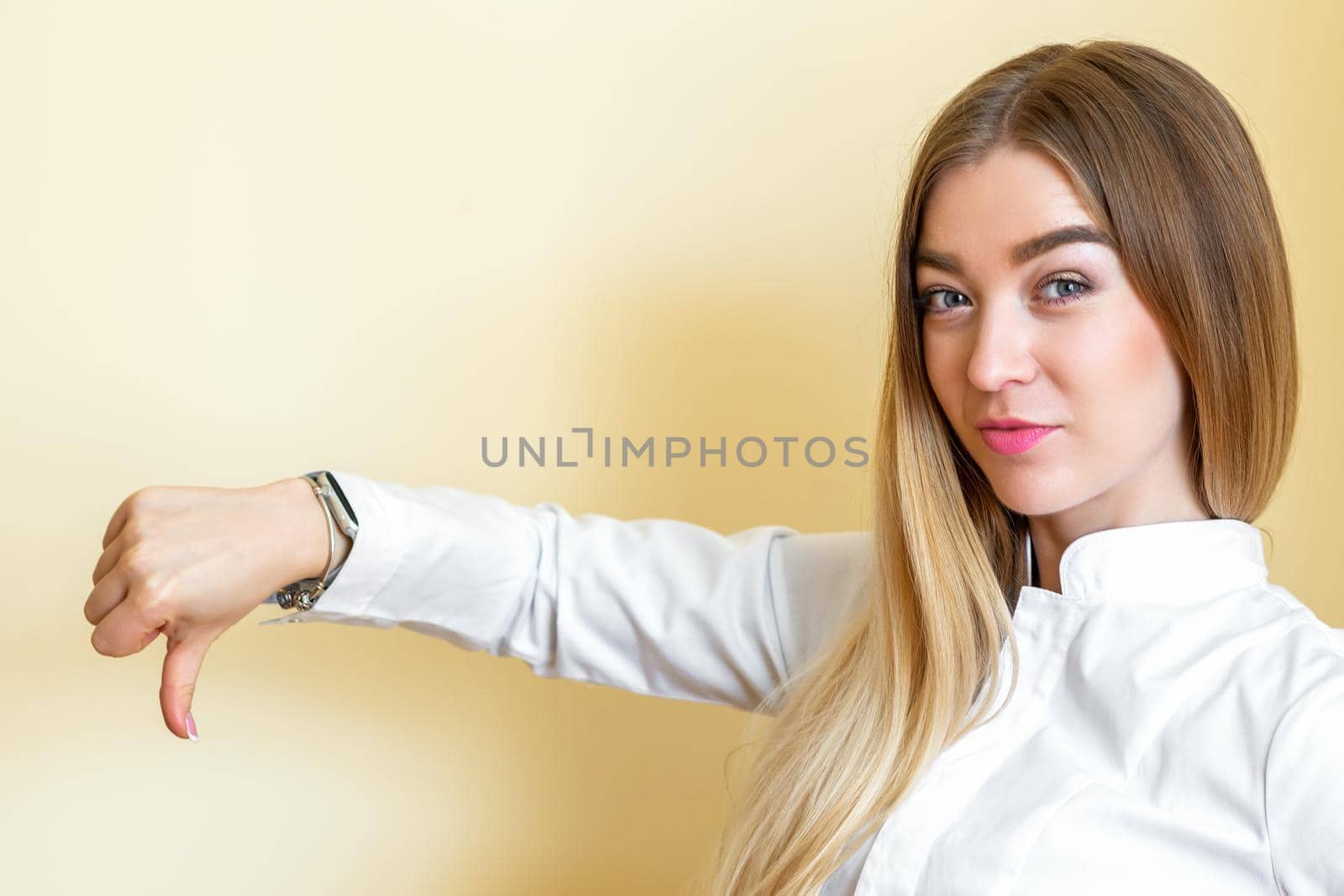 A woman showing dislike. Young beautiful businesswoman wearing a white shirt with thumb down isolated over a yellow background