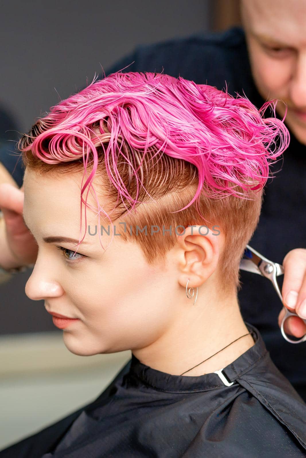 Woman having a new haircut. A male hairstylist is cutting dyed pink short hair with scissors in a hair salon. by okskukuruza