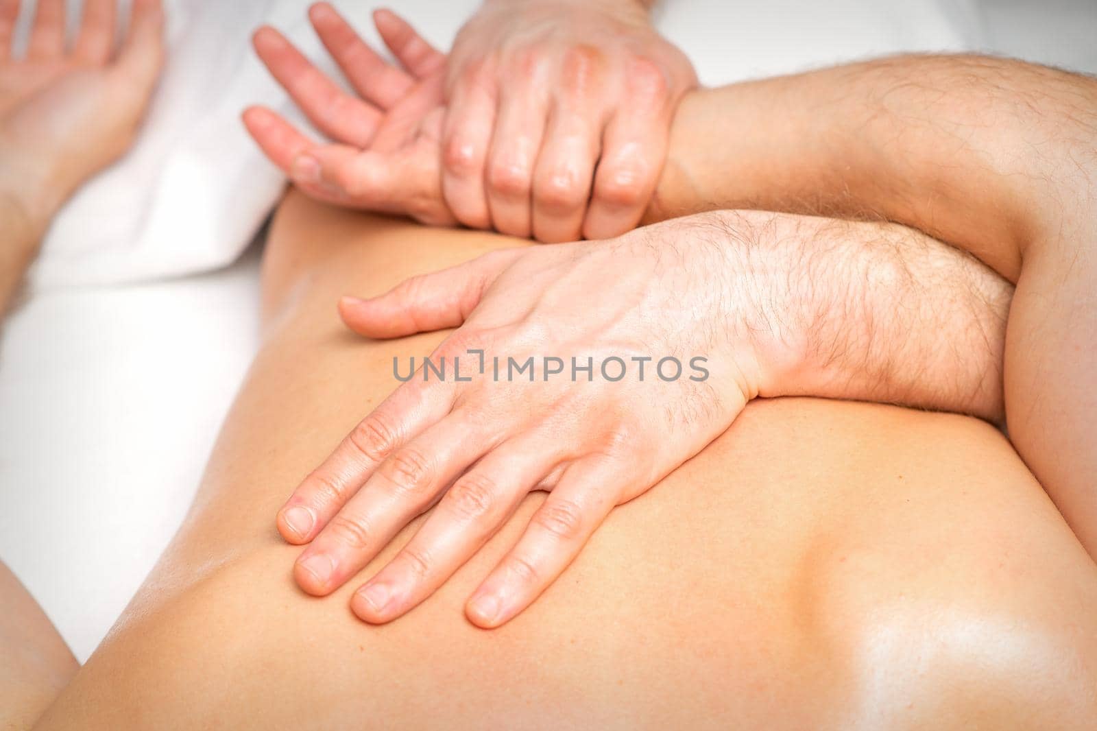 A male physiotherapist stretches the arms on the back of a man lying down, close up