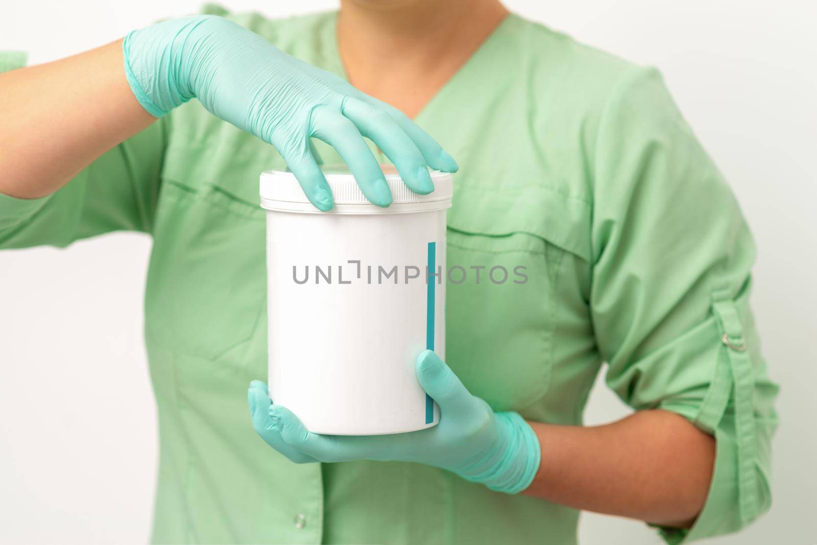 Hands in protective gloves of beautician open a white body cream jar on white background