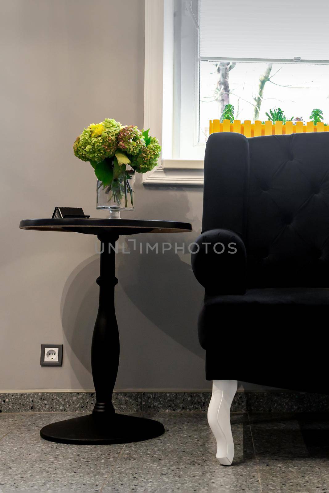 Interior of the beauty room. Black sofa with small yellow pillows and coffee table on a gray wall background with a window