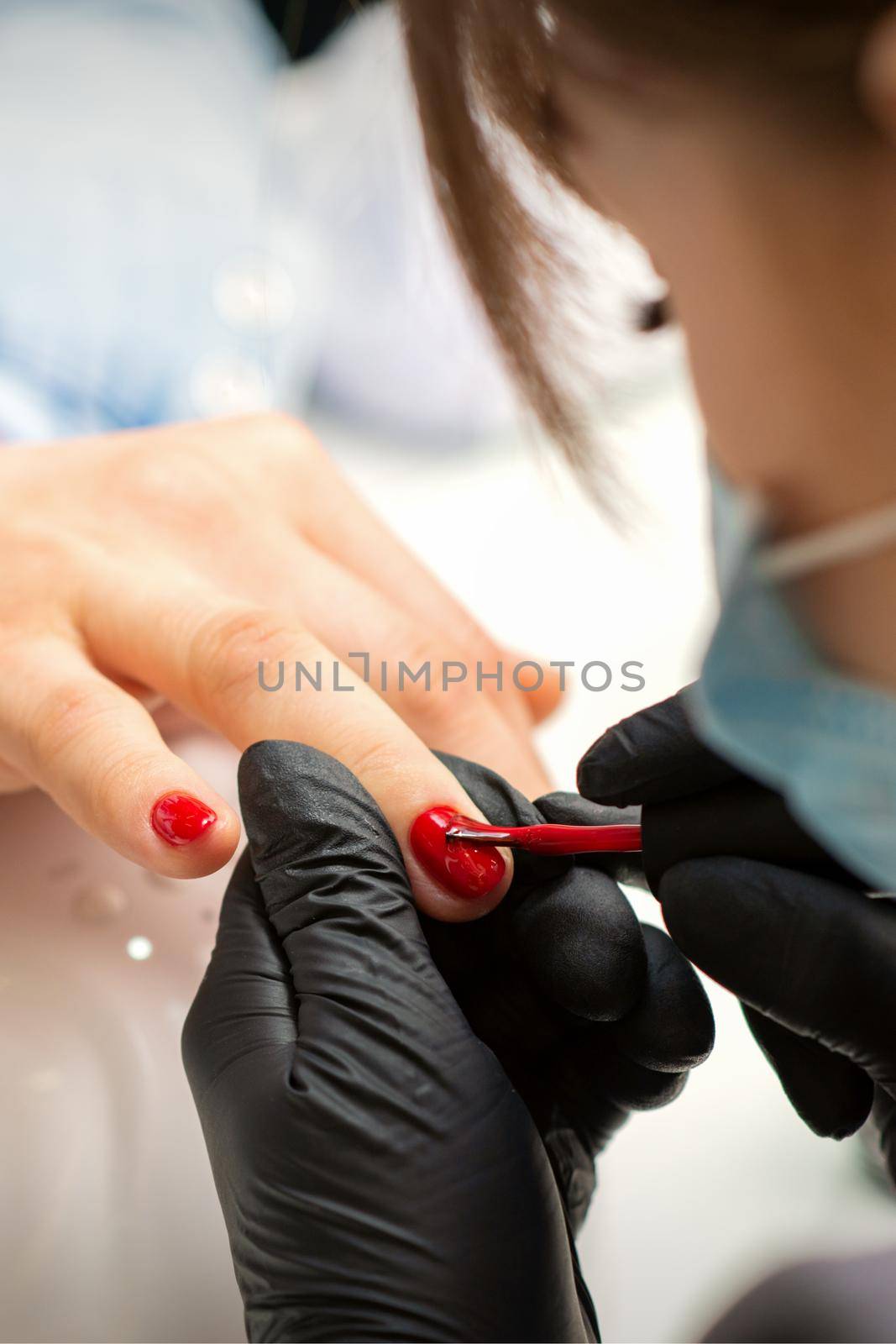 Painting nails of a woman. Hands of Manicurist in black gloves applying red nail polish on female Nails in a beauty salon