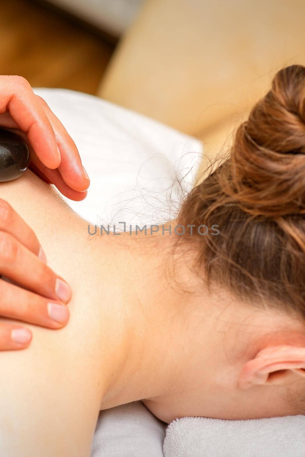 Hot stone massage therapy. Caucasian young woman getting a hot stone massage on back at spa salon