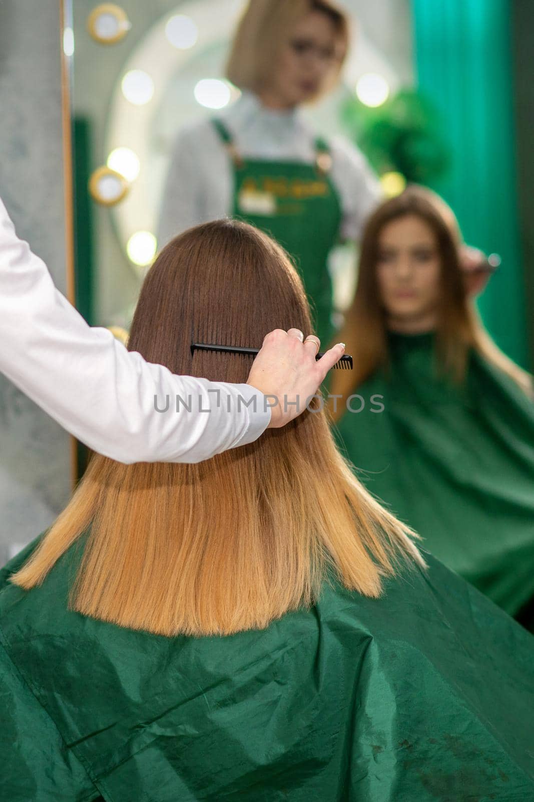 A female hairdresser is combing the long brown hair of a young woman at a parlor