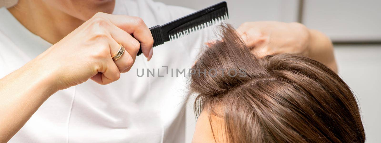 Professional hairdresser doing hairstyle for a beautiful brunette young woman with long hair. Concept of fashion and beauty