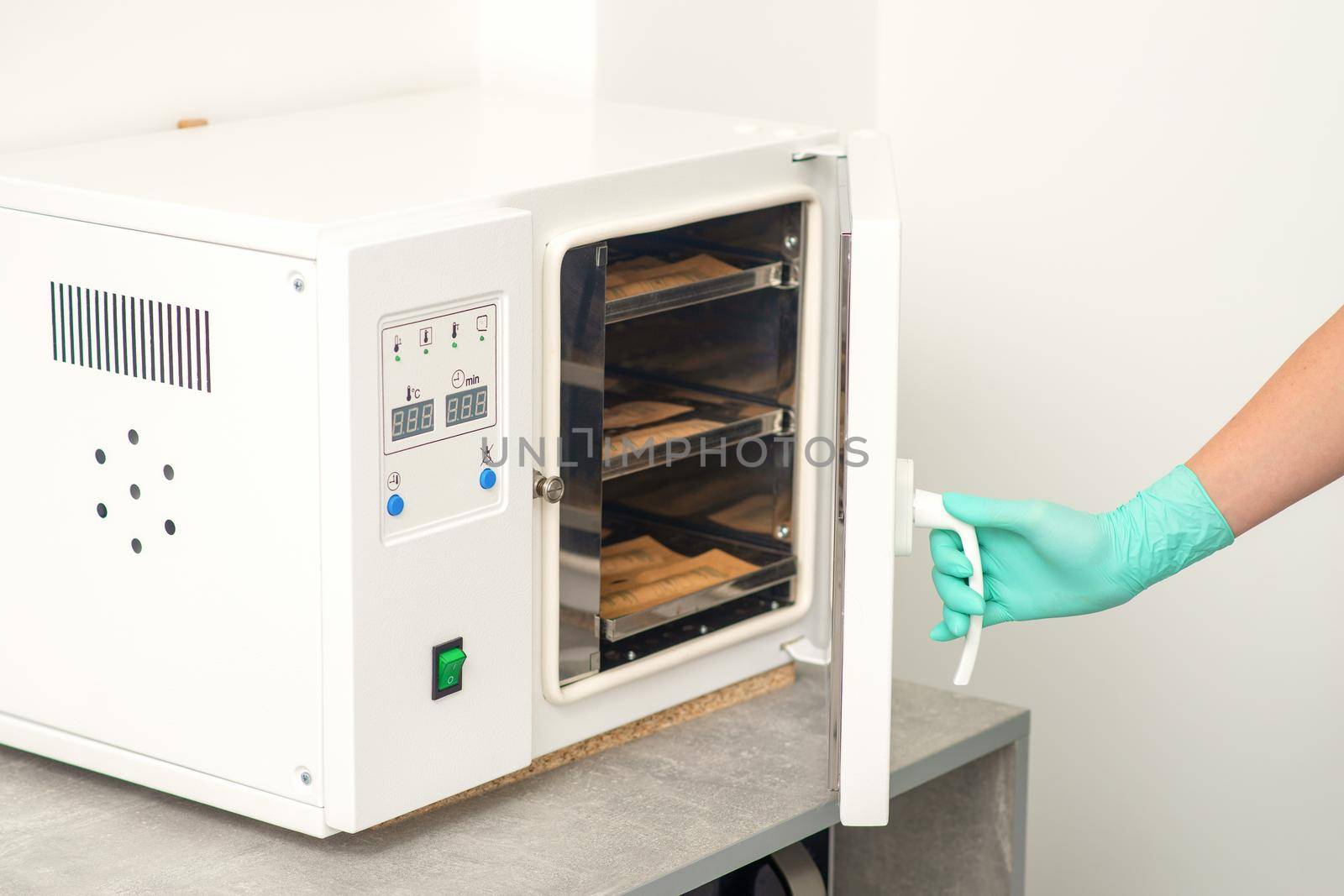 Beautician in protective gloves close the door of the machine for disinfection of tools before the depilation procedure. by okskukuruza