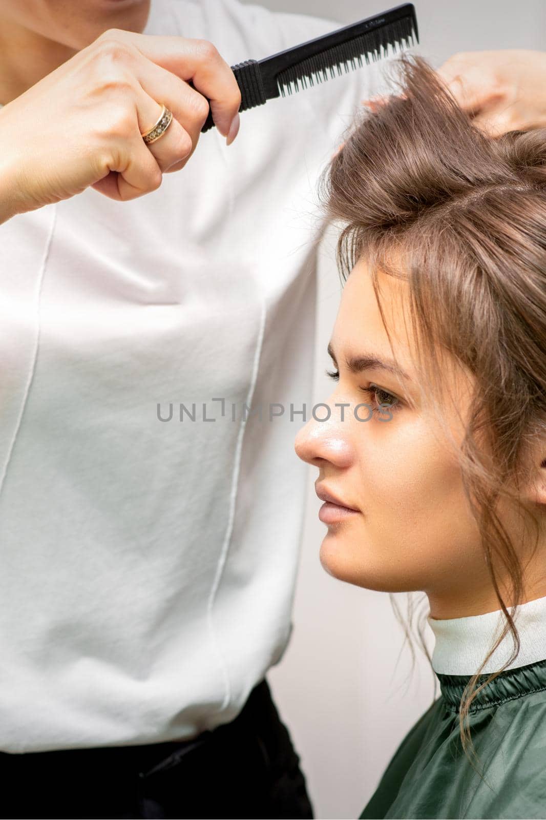 Professional hairdresser doing hairstyle for a beautiful brunette young woman with long hair. Concept of fashion and beauty