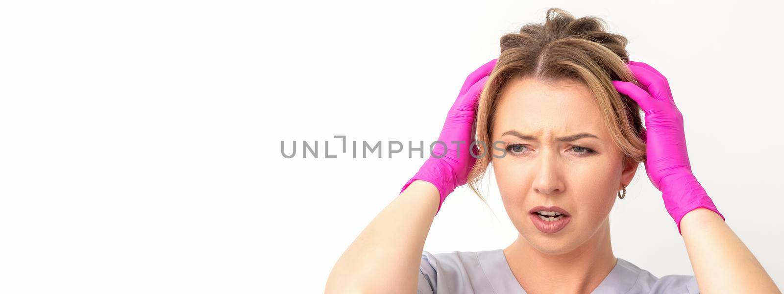 The emotionally shocked young female medical worker holding hands on her head fell into panic on white background, infection, epidemic, virus, and disease concept