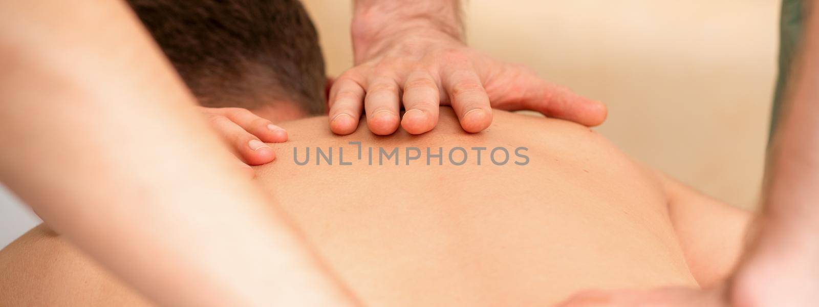 Young man receiving back massage in four hands in spa beauty salon. by okskukuruza