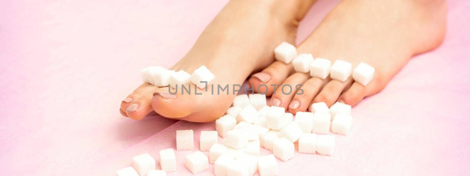 Sugar cubes lying in a row on female feet on pink background with copy space, depilation concept