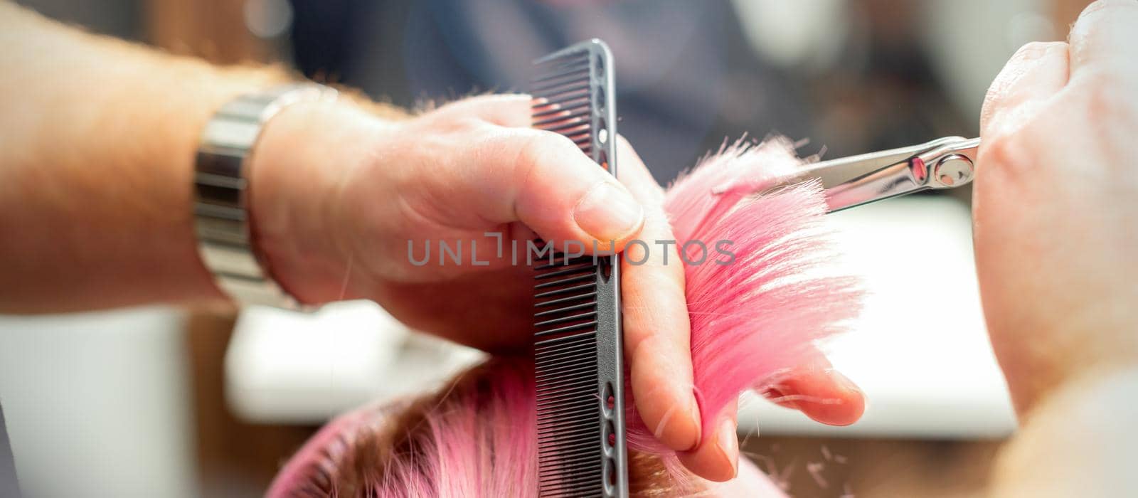 Woman having a new haircut. Male hairstylist cutting pink hair with scissors in a hair salon, close up