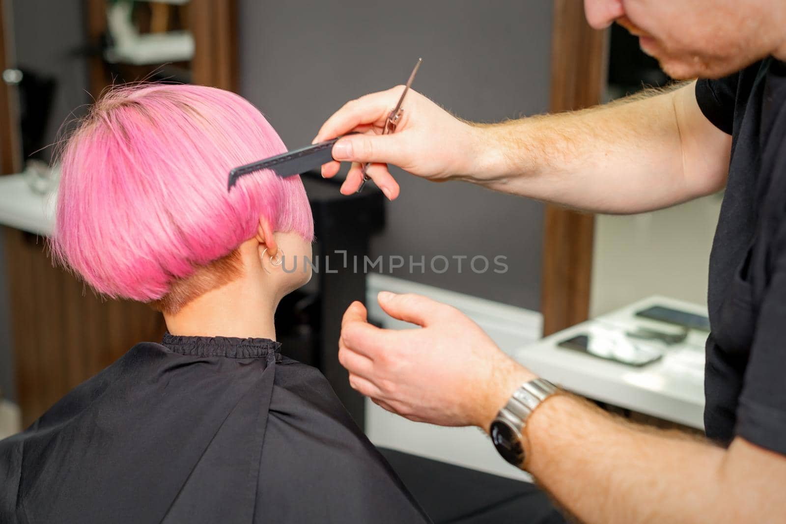 Hands of hairdresser combing hair making short pink hairstyle for a young caucasian woman in a beauty salon