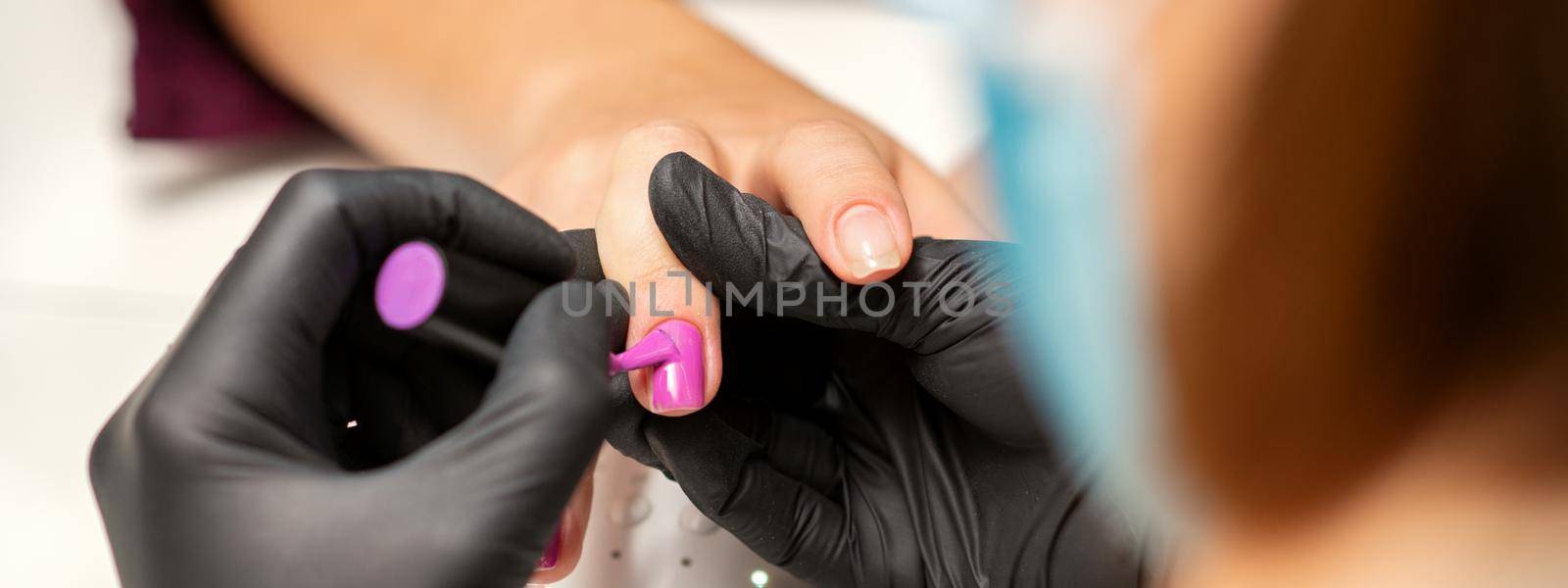 Painting nails of a woman. Hands of Manicurist in black gloves applying pink nail polish on female Nails in a beauty salon. by okskukuruza