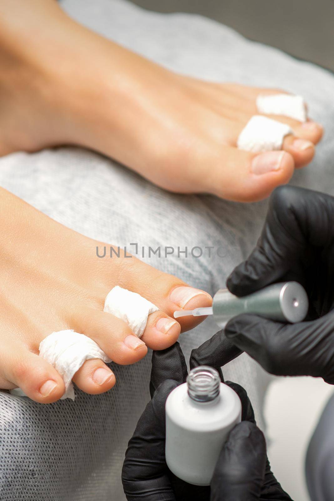 Pedicurist applying transparent varnish to the female toenails in a beauty salon. by okskukuruza