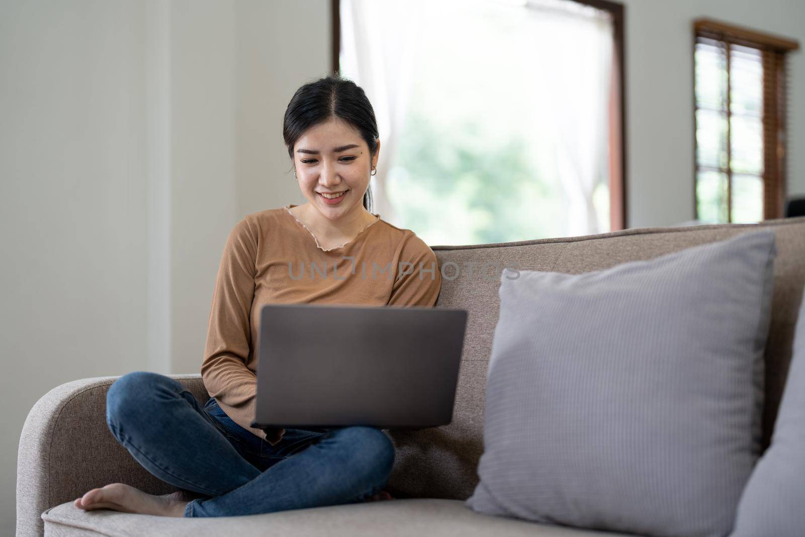 Happy asian woman using laptop in the sofa with a happy face standing and smiling with a confident smile showing teeth.