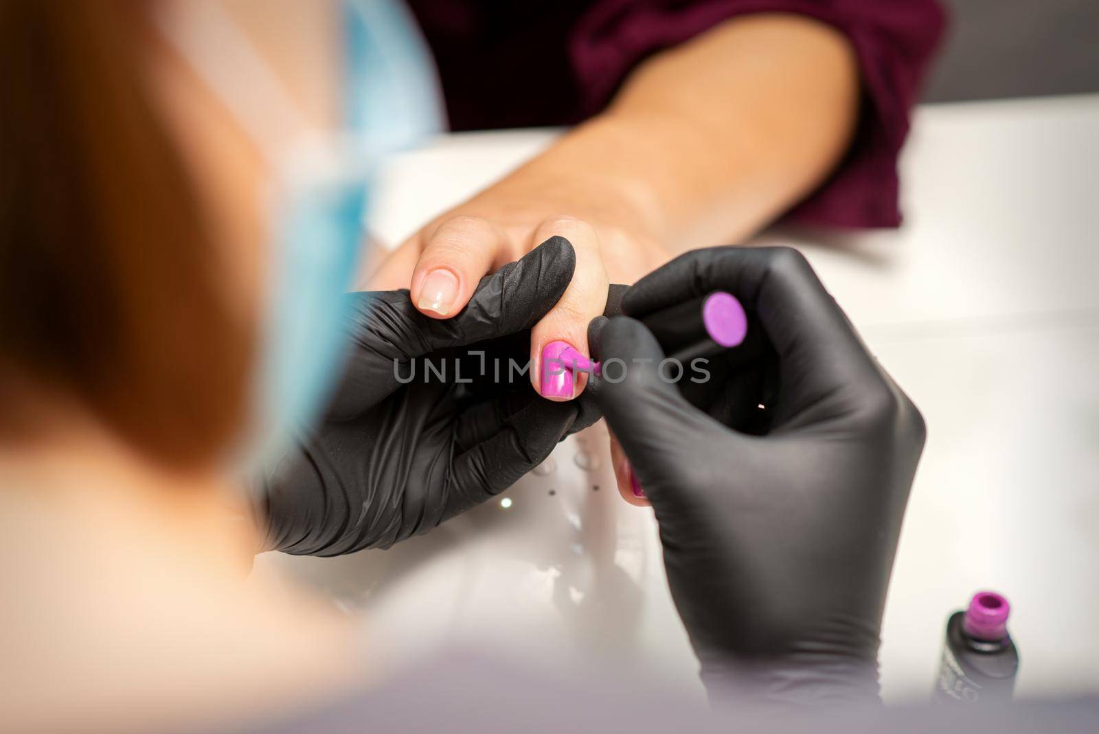 Painting nails of a woman. Hands of Manicurist in black gloves applying pink nail polish on female Nails in a beauty salon