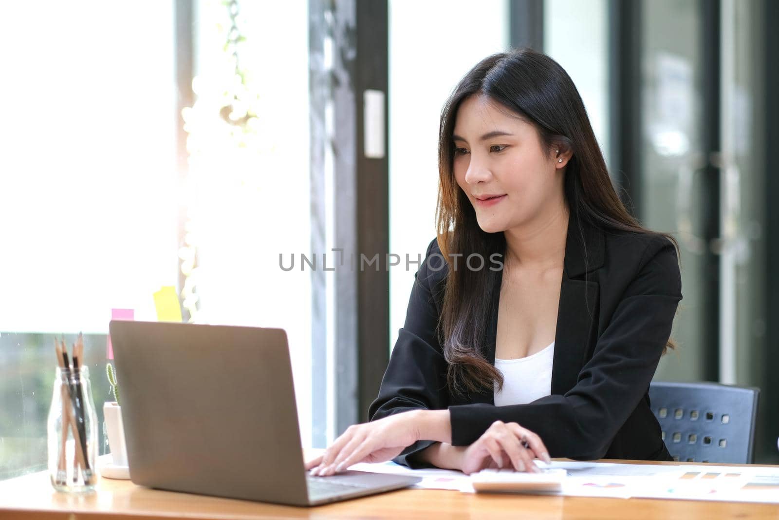 Young Asian businesswoman using a calculator to calculate business principles. Accounting statistics concept at the office. by wichayada