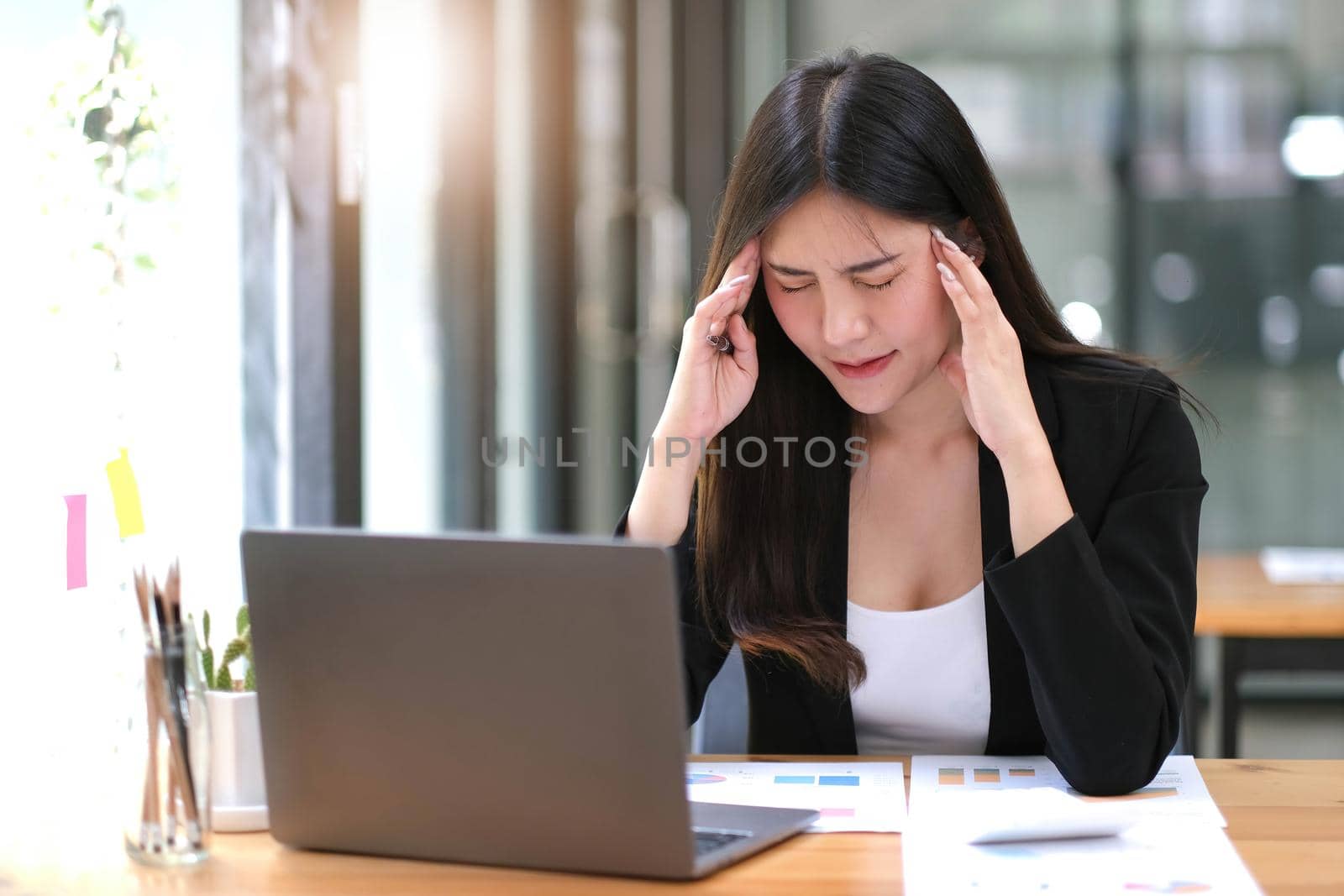 Young Asian woman feeling migraine head strain. Tired, Overworked businesswoman financier while working on laptop computer in office..